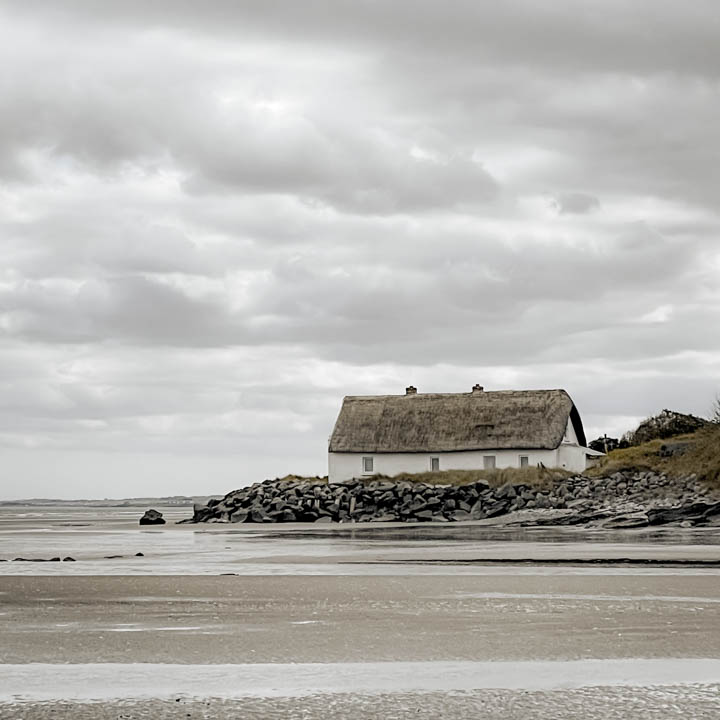 Thatched Nanny Cottage in Laytown, Co Meath beside a calm Irish beach under soft, overcast skies.