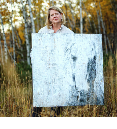 Artist Clare O'Neill holding a large abstract encaustic painting of a horse outdoors in an autumn landscape, with birch trees and golden foliage in the background, showcasing contemporary mixed-media artwork.